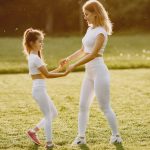 A mother and daughter in matching activewear enjoy playful bonding at the park during sunset.